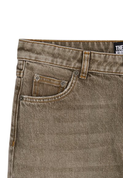 Jeans in denim marrone con una tasca frontale a sinistra, caratterizzati da cuciture arancioni chiare e rivetti in metallo, tessuto testurizzato con un motivo sottile.