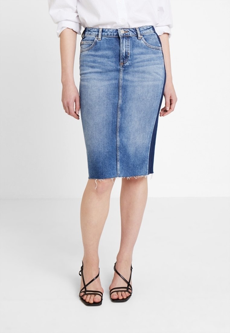 Denim pencil skirt in light blue with a frayed hem, featuring a dark blue side panel and five belt loops. Paired with strappy black heels.