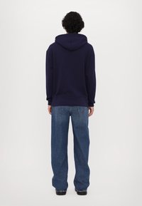 Sudadera azul marino con capucha ajustable, de corte holgado, combinada con unos vaqueros de pierna ancha de color azul claro. La tela parece suave, con puños y dobladillo acanalados.
