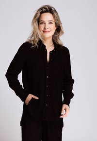 Schwarzes Cordhemd mit langen Ärmeln, durchgehendem Knopfverschluss und Brusttasche. Strukturierter Stoff und lockere Passform.