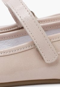 Světle růžová lakovaná bota s páskem přes nárt, prošívané detaily podél okrajů a hladký, lesklý povrch.