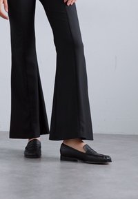 Zwarte flare-pantalons met een gladde textuur, gecombineerd met zwarte instappers met een gestikt ontwerp en een vlakke zool.