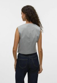Grå ärmlös topp med en strukturerad design, croppad längd, slät textur och en söm bak. Matchad med mörka jeans med fickor.
