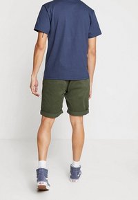 Laivastonsininen puuvillapaita, vihreät käärityt shortsit, valkoiset nilkkasukat ja siniset lenkkarit. Korosta rentoa istuvuutta ja epämuodollista ulkoilutyyliä.