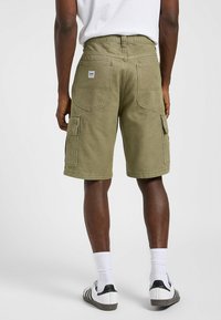 Shorts cargo vert olive en mélange de coton, dotés de deux poches arrière et de poches latérales. La ceinture est équipée de passants de ceinture et d'une étiquette.