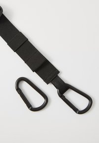 Musta nailonihihna, jossa on mustat metalliset karabiinit kummassakin päässä; siinä on teksturoitu pinta ja kolme säädettävää osiota.