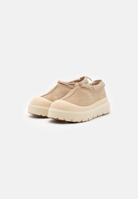 Beige Wildlederschuhe mit einer strukturierten Netz-Zehenkappe, runder Silhouette und einer dicken, geriffelten Sohle. Weicher Kragen und elastische Öffnung für einfaches An- und Ausziehen.