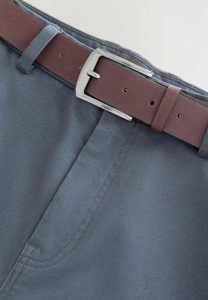 Tumedad sinised püksid, millel on siledad tekstuur ja nähtavad õmblused, on kombineeritud pruuni nahavöö ja poleeritud hõbedase pandliga.