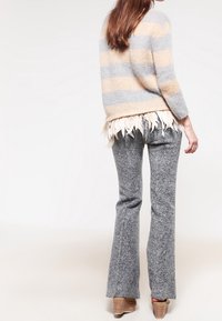 Grau-beige gestreifter Pullover mit einem Federbesatz, kombiniert mit grauen Schlaghosen aus strukturiertem Stoff und hellbraunen Absatzschuhen.
