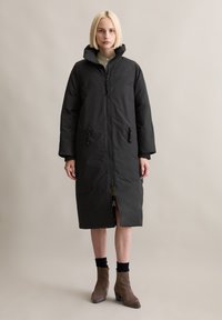 Schwarzer, gesteppter langer Mantel mit Reißverschluss, verstellbaren Kordeln in der Taille und seitlichen Taschen. Hat einen hohen Kragen und einen geschlitzten Saum.