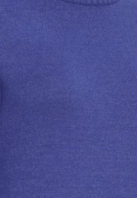 Gros plan sur un tissu doux et tricoté de couleur bleu roi uni avec un motif côtelé subtil près du bord supérieur.