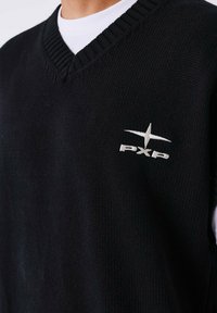 Suéter negro de punto sin mangas con diseño de cuello en V, que presenta un logotipo bordado en blanco "PXP" y un detalle de estrella en el pecho.
