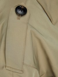 Khaki-Stoff mit glatter Textur, ausgestattet mit einem auffälligen schwarzen Knopf und schrägen Taschen, die maßgeschneiderte Designelemente hervorheben.