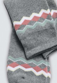Calcetines grises con un patrón de zigzag en rojo, verde, rosa y blanco. Hechos de una tela suave con una textura lisa y un tejido uniforme.