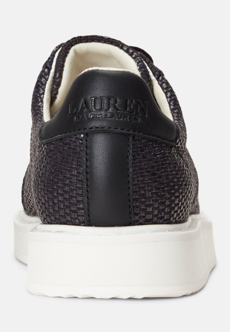 Baskets noires avec un dessus en tissu tissé, semelle en caoutchouc blanche et un accent en cuir noir au niveau du talon avec un logo en relief.