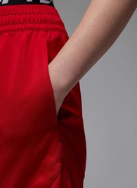 Røde sportsshorts har en elastisk talje og sidelommer. Nærbillede viser det glatte stof og den afslappede pasform.