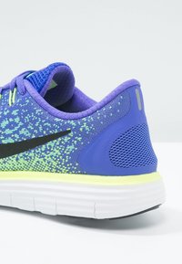 Chaussure de course bleue avec une tige en mesh texturé agrémentée de détails verts, un logo noir et une semelle rembourrée avec un contour jaune.
