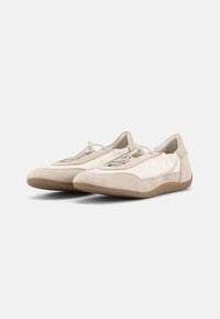 Ζευγάρι μπεζ casual παπουτσιών χωρίς κορδόνια με σουέτ λεπτομέρειες και ελαστικά κορδόνια με κούμπωμα, εμφανίζεται σε λευκό φόντο.