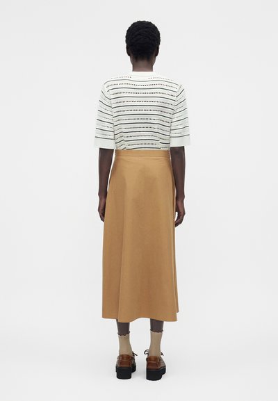 Άτομο που φοράει λευκό πλεκτό τοπ με κοντά μανίκια και οριζόντια ανοίγματα, μπεζ midi φούστα με ψηλή μέση, μπεζ κάλτσες και καφέ πλατφόρμες, από πίσω.