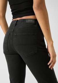 Zwarte denim jeans met een slim fit ontwerp, voorzien van achterzakken en een gestructureerde afwerking. Label met "STR" op de tailleband.