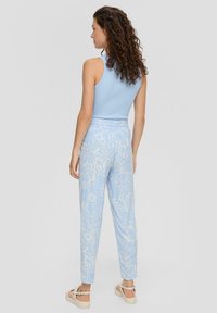 Helles blaues Tanktop kombiniert mit gemusterten Hosen, die florale Designs in Creme aufweisen. Die Hosen haben einen elastischen Bund und schmale Beine.