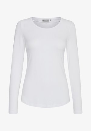 Balta garo piedurkņu krekls, kas izgatavots no gludas kokvilnas ar noapaļotu kakla izgriezumu un taisnu griezumu. Iezīmē minimālu šuvju daudzumu un nav rotājumu.