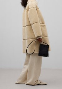 Beige fleecejacka med en boxig design, med stickade paneler. I kombination med krämfärgade vida byxor och en svart crossbody-väska.