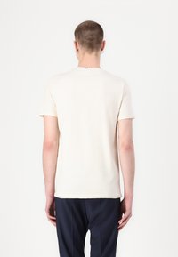 Tricou crem cu mânecă scurtă, guler rotund, textură netedă, tiv drept și un design minimalist. Prezintă un mic accent de culoare la guler.