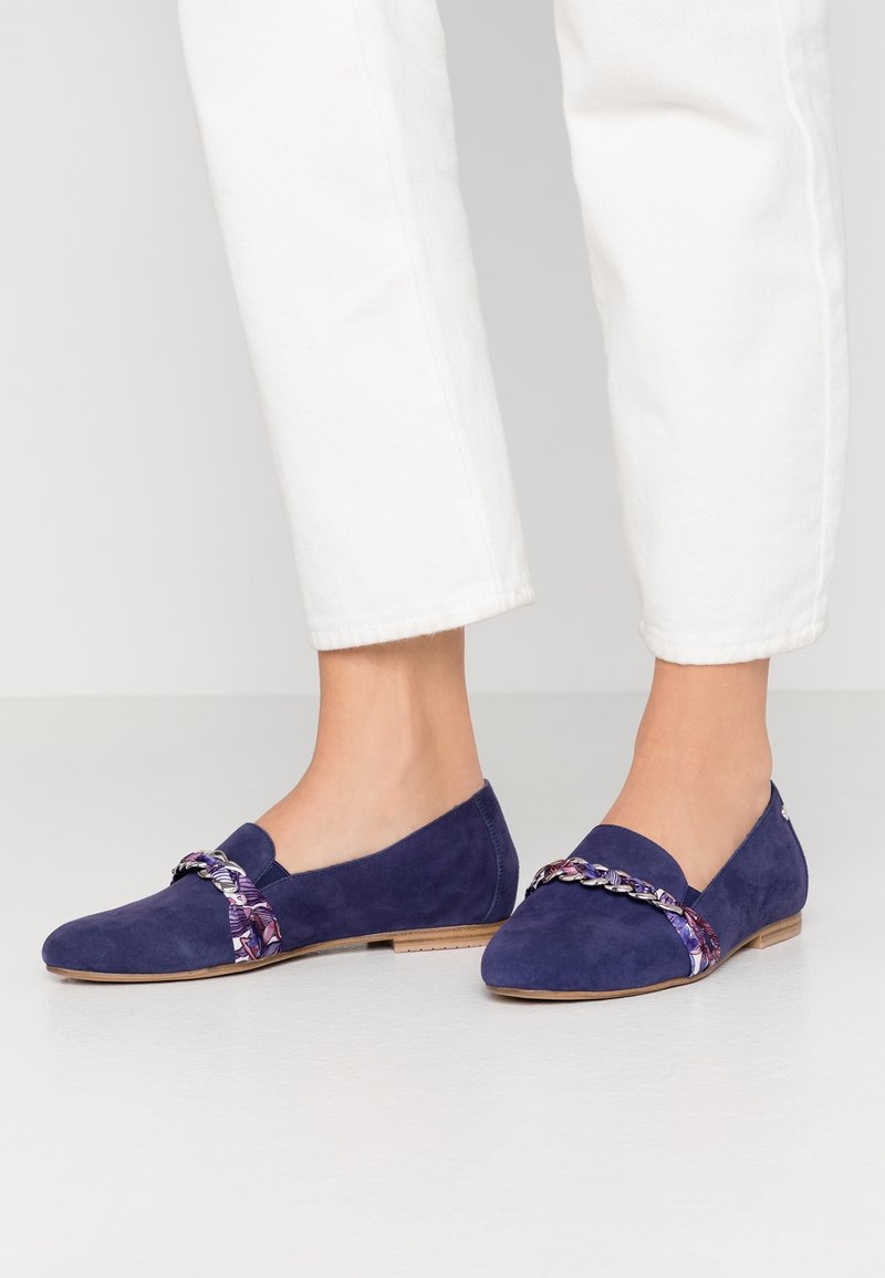 Mocassins en suede bleu marine avec semelles plates présentent un accent floral tressé violet sur le devant, offrant un contraste texturé.
