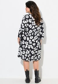 Schwarzes Kleid mit weißem Blumendruck, Dreiviertelärmel, geschichteter Rock und tailliertem Schnitt. Kombiniert mit schwarzen, mit Nieten besetzten Ankle Boots.