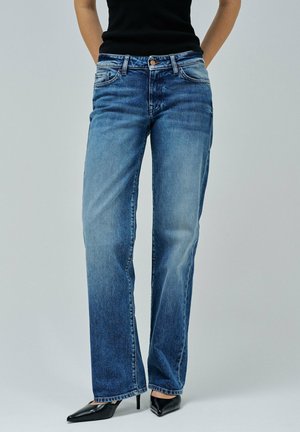 Jean droit bleu clair en denim, avec un design classique à cinq poches et un léger dégradé. Porté avec des talons noirs à bout pointu.