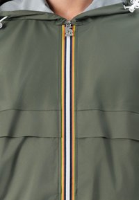 Giacca leggera verde con zip a tutta lunghezza e un accento a righe arcobaleno, cappuccio con stringhe e texture liscia.