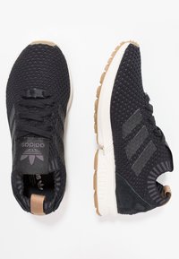 Zwarte sportschoenen met een gestructureerde mesh bovenkant, rubberen zool en drie diagonale strepen. Voorzien van een geveerd hiel en een contrasterende gumzool.