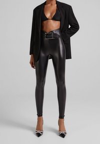 Svarta fuskläder leggings med hög midja och bredt bälte. Kombinerat med en svart kortad bikinitopp och en svart blazer.