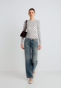 Pitkähihainen valkoinen paita mustilla pilkuilla, haalistuneet siniset leveälahkeiset farkut ja beiget kengät. Mukana pieni ruskea käsilaukku.