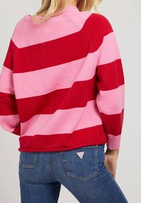 Pull rayé rouge et rose avec un col rond, des manches longues et des poignets côtelés. Associé à un jean en denim bleu avec un détail de logo.