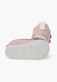 Scarpe di pelle rosa con suola in gomma bianca. Presentano una fascia con chiusura a strappo e un colletto imbottito. Accento testurizzato sul lato.