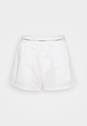 White cotton boxers with an elastic waistband featuring "Calvin Klein" branding in gray. Classic design with a loose fit and side pockets.