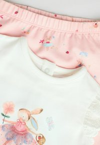 Chemise blanche à manches courtes avec un graphisme de lapin et un pantalon de pyjama rose ornés de motifs floraux et de lapins sur fond rose clair.