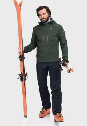 Green waterproof jacket, orange skis, black pants, and orange ski boots. Skis have black bindings. Smooth fabric, sporty design.