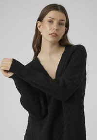 Maglione nero lavorato a maglia con scollatura a V profonda e polsini a costine, caratterizzato da motivi testurizzati diagonali sul tessuto. Materiale morbido e caldo.