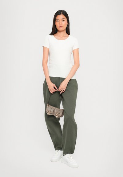 Witte geribbelde top met korte mouwen, losse olijfgroene broek, grijze crossbody tas met gouden accenten en witte sneakers.