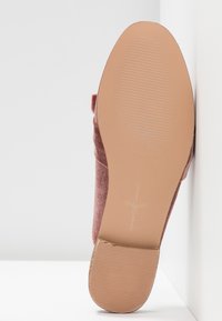 Semelle d'une chaussure plate rose avec talon texturé et avant lisse, taille 37, positionnée verticalement contre un mur d'angle blanc.