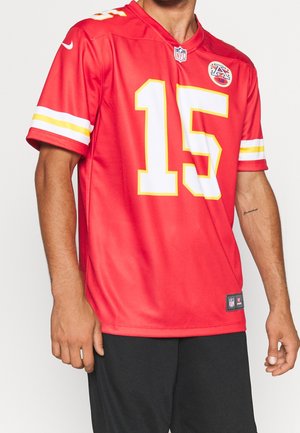Mann trägt ein rotes NFL Kansas City Chiefs Football-Trikot mit der Nummer 15 und schwarzen Shorts vor einfarbigem Hintergrund.