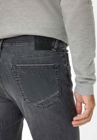 Grijze denim jeans met een zwart leren label met de tekst "Brax." Kenmerken zijn een aangesloten pasvorm en subtiele vervaging op de benen.