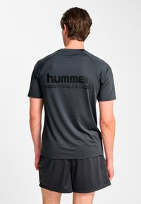 Szara sportowa koszulka o siateczkowej fakturze z krótkimi rękawami, z czarnym logo "hummel PERFORMANCE" na plecach. W zestawie z czarnymi szortami.