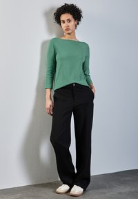 Haut vert à côtes avec des manches trois-quarts, associé à un pantalon large noir et des baskets blanches. Design minimaliste et moderne avec des lignes épurées.