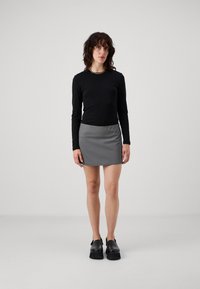 Top nero a maniche lunghe, minigonna grigia, scarpe con plateau nere. Tessuto liscio, design aderente, stile minimalista con cuciture laterali.
