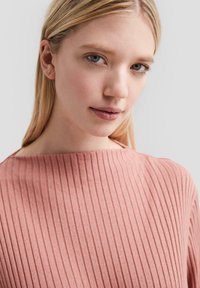 Hellrosa, gerippter Pullover mit hohem Kragen, glatter Textur und dezentem Glanz, der eine lockere Passform und minimale Nähte aufweist.