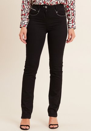Zwarte skinny jeans met een gladde textuur, voorzien van pockets met metalen accenten en een aansluitend ontwerp. Gecombineerd met zwarte hakken met bandjes.